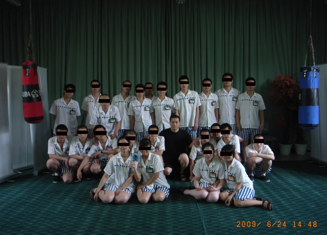 少年犯与艺术家李牧的集体合影：约二十人分两排站坐，李牧居中，前排一女孩手持一张CD，所有少年脸部打码。