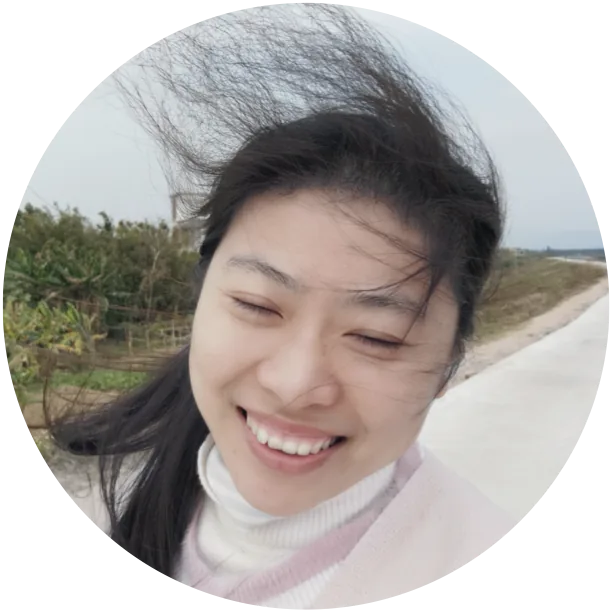 安超在户外的笑脸自拍圆形头像，身后是乡间小路与农田，长发被风吹起。