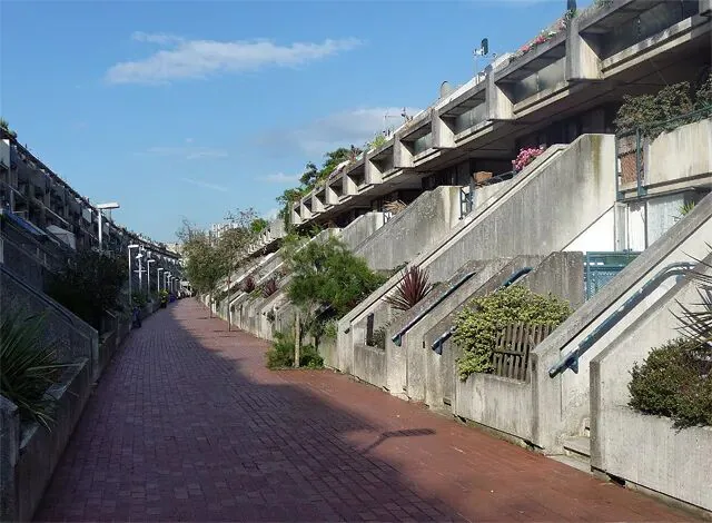 阶梯状混凝土住宅楼沿红砖步道两侧排列,各户露台种满绿植,是典型的粗野主义风格住宅区实景。