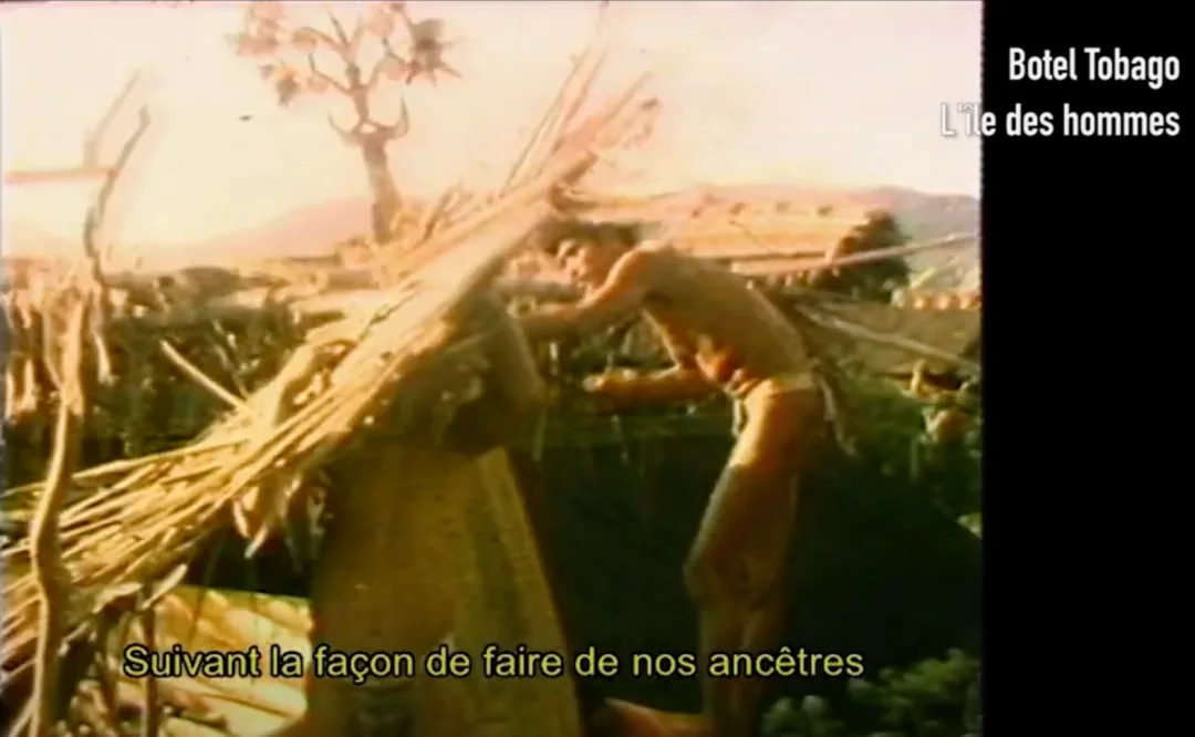 纪录片截图,右上角片名文字「Botel Tobago / L'île des hommes」,字幕「Suivant la façon de faire de nos ancêtres」,画面中一名男子在搭建木架结构