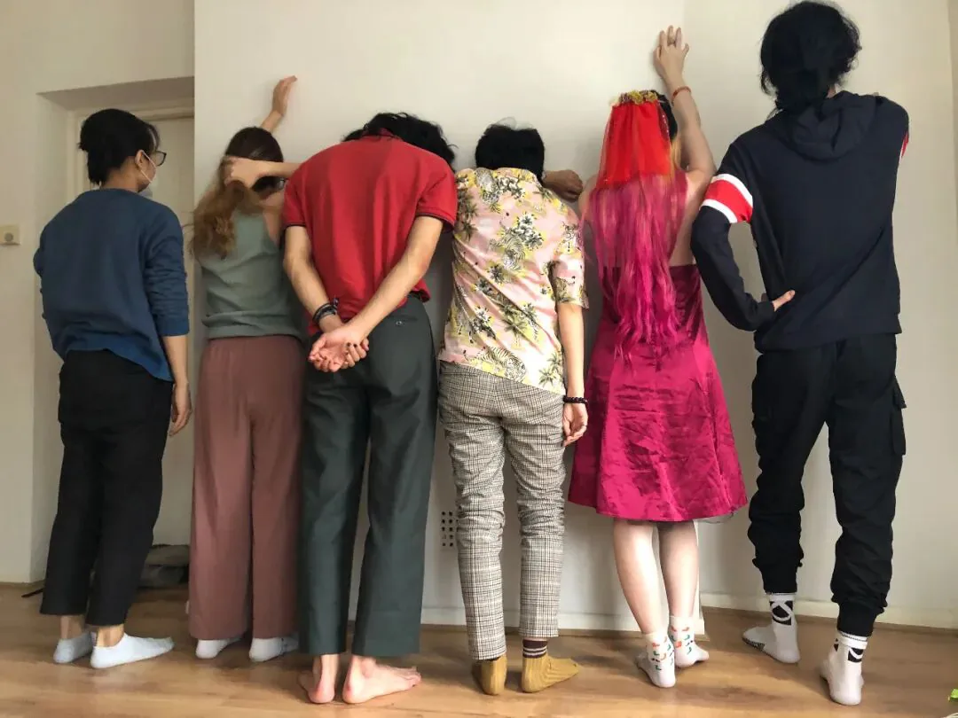六人背对镜头面墙而立,一手扶墙,服饰各异,姿态统一。