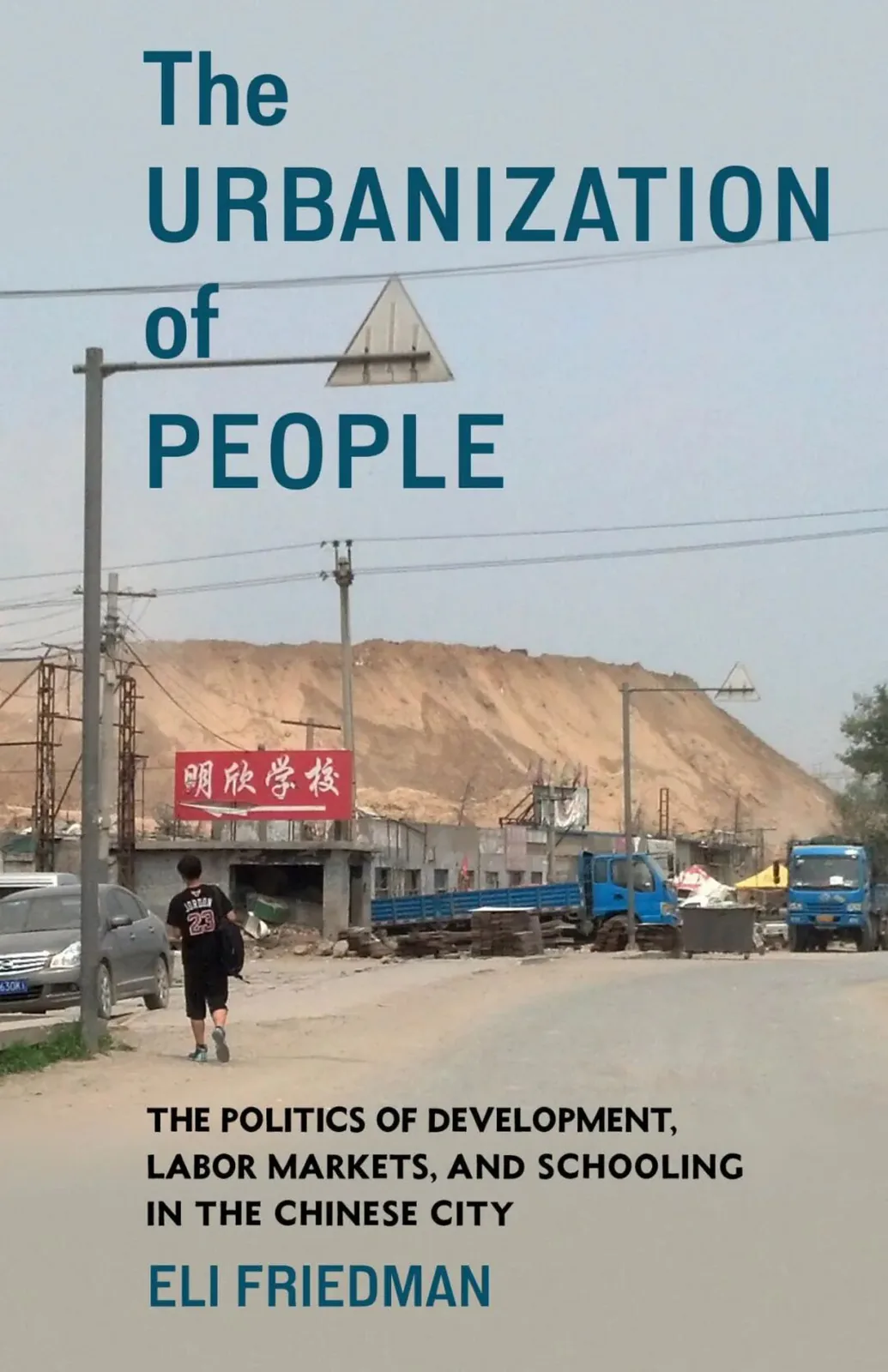 封面照片为尘土飞扬的城郊道路，一名男孩背着书包独自走过，路边停着卡车，红色招牌写着“明欣学校”，背景是巨大的沙土堆；上方印着书名《The Urbanization of People》及作者 Eli Friedman。