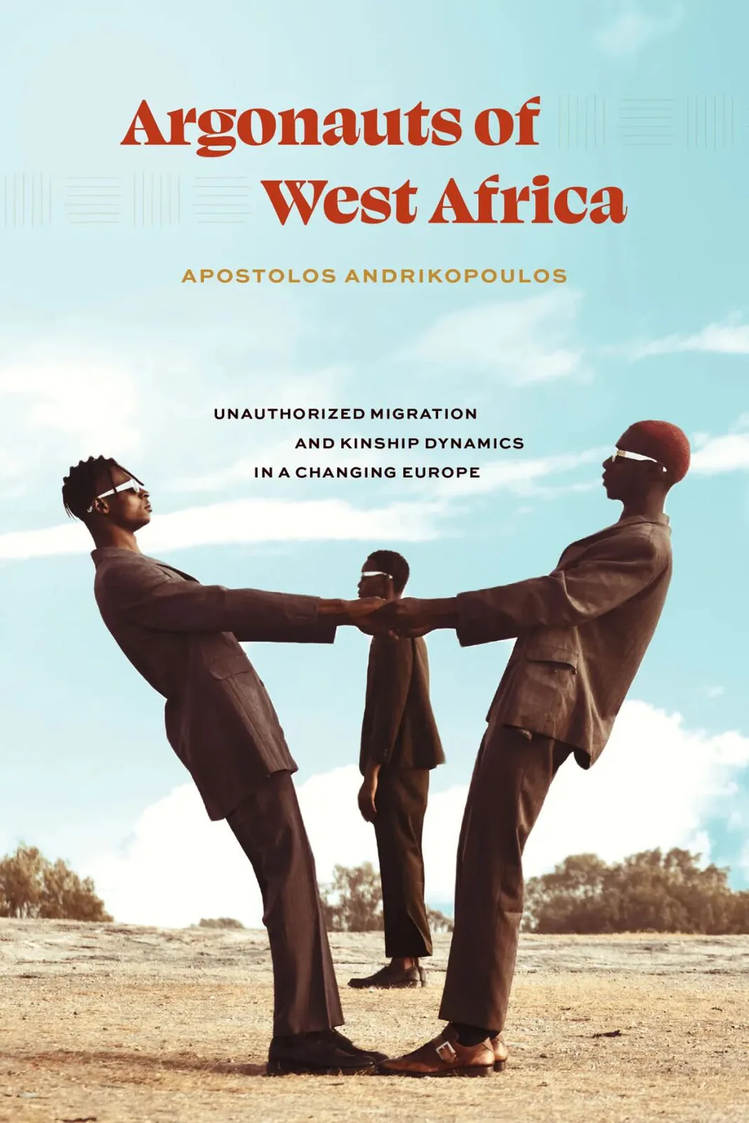 《西非的航海者》（Argonauts of West Africa）封面，两名身着西装的男子在沙地上向后倾身、以手相牵保持平衡，身后一人站立，背景是蓝天绿树。作者阿波斯托洛斯·安德里科普洛斯。