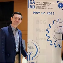 一名男子身穿西装，站在写有“全球无障碍宣传日 GAAD MAY 17, 2022”字样的展板旁留影。