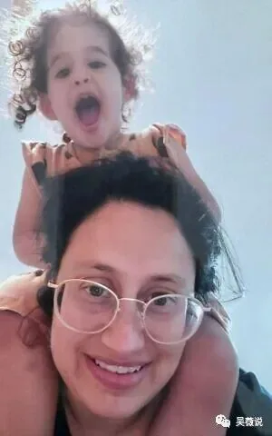 一名戴眼镜的女性与骑在她肩头的卷发幼童合影自拍，两人笑容灿烂。