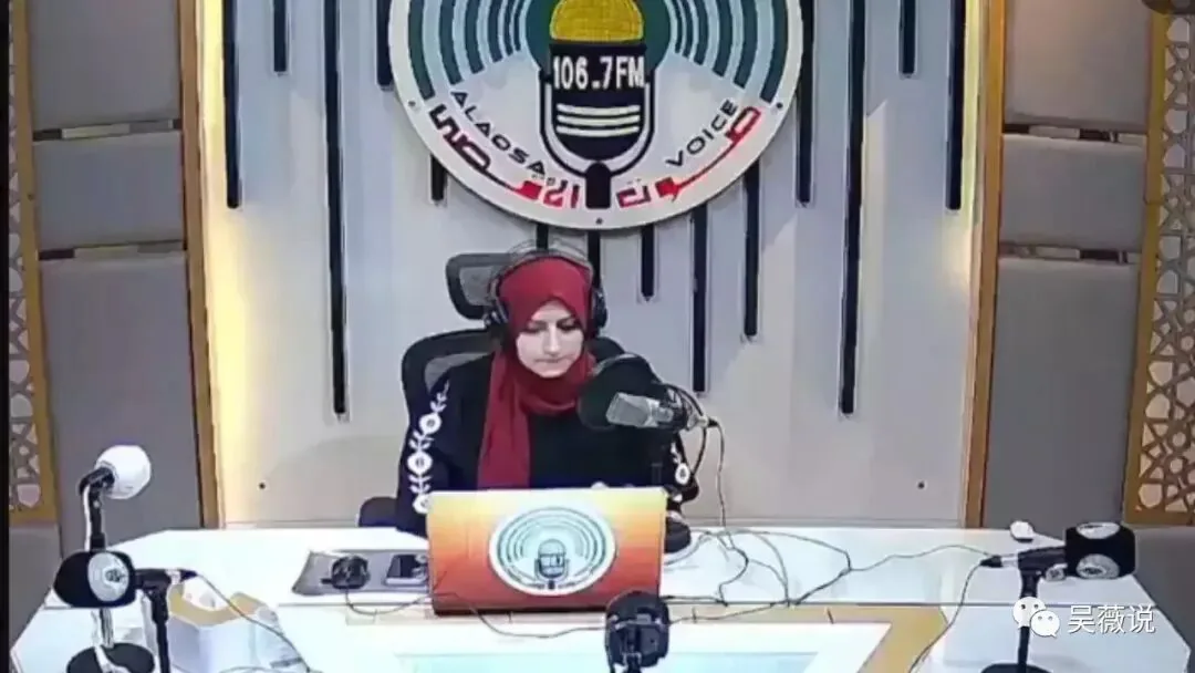 杜阿·沙拉夫戴红色头巾与耳机，坐在阿克萨之声106.7FM广播台前工作。