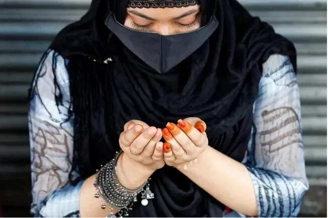 特写镜头下，一名戴黑色面纱的妇女双手合十做祈祷手势，手腕戴银色手镯，指甲染成橙色。