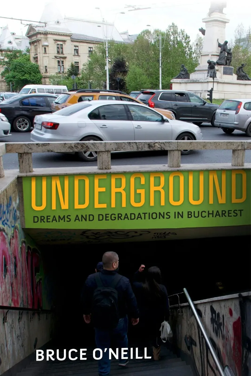 书封《Underground: Dreams and Degradations in Bucharest》，作者 Bruce O'Neill；街景照片，上方车流穿行的马路与身后欧式建筑，两人背影正走下涂满涂鸦的地下通道台阶，入口处绿色招牌写着书名。