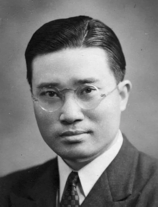 戴圆框眼镜、穿深色西装打领带的年轻男子面部特写，梳背头，表情严肃，柔光影棚背景。
