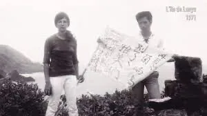 黑白老照片，两人站在海边礁石旁，一人展开一张写满字迹的大幅纸张，图片右上角水印文字「L'île de Lanyu 1971」