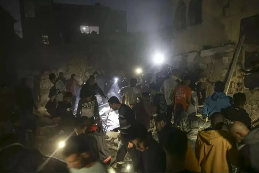 夜间场景，一大群人手持手电筒和手机灯光，在倒塌建筑的瓦砾堆中搜寻，周围是漆黑的废墟和残垣。
