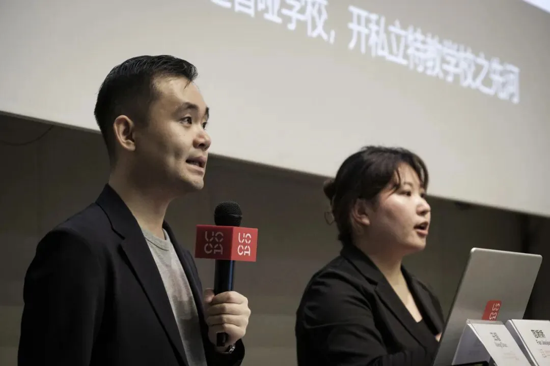 王超手持UCCA话筒讲话,身旁范娇娇打手语翻译,两人身后大屏幕可见部分讲座文字。
