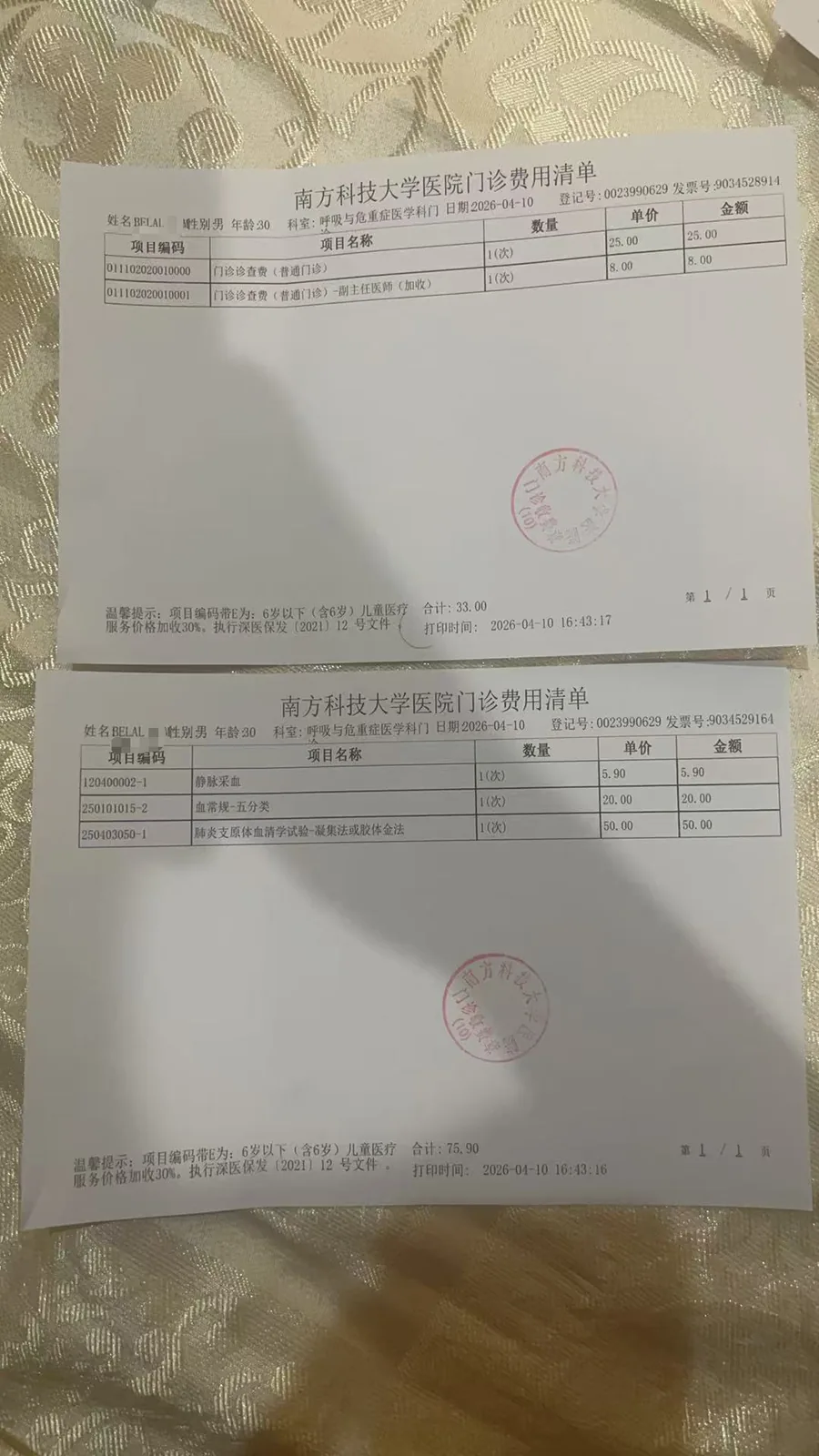 两张南方科技大学医院门诊费用清单摆放在织物上，分别记录挂号费、诊查费等门诊收费项目及金额，并盖有医院印章。