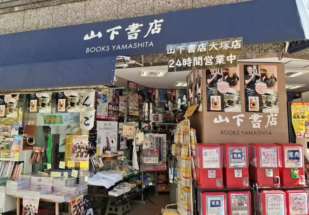 东京一家名为“山下書店”（BOOKS YAMASHITA）的24小时营业书店门面，门口摆满杂志书刊，旁边放着多台红色扭蛋机。