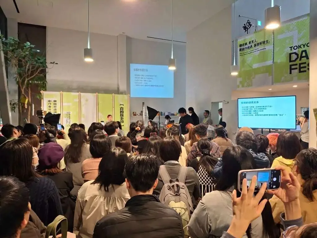 拥挤的会场内座无虚席，不少观众站立听讲并举起手机拍照，讲台旁投影着写满文字的演讲提纲，墙上挂着绿色“故事节”主视觉海报。