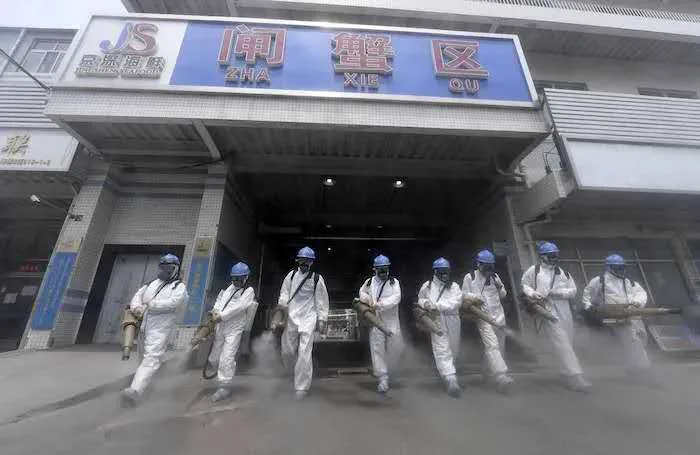 八名身穿白色防护服、戴蓝色头盔的工作人员手持喷雾器,从写有'闸蟹区'招牌的市场入口列队走出,喷洒消毒雾气。