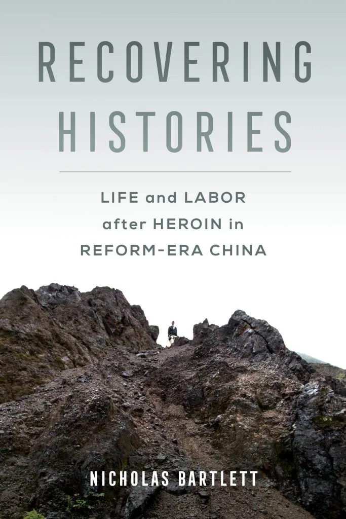 书封，灰绿色调，一人站在嶙峋山脊小径上，书名《Recovering Histories: Life and Labor after Heroin in Reform-Era China》，作者Nicholas Bartlett。