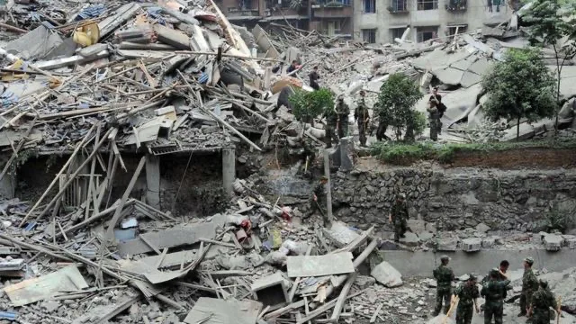 汶川地震后倒塌的多层建筑化为一片废墟，多名迷彩军装士兵在瓦砾间搜救。