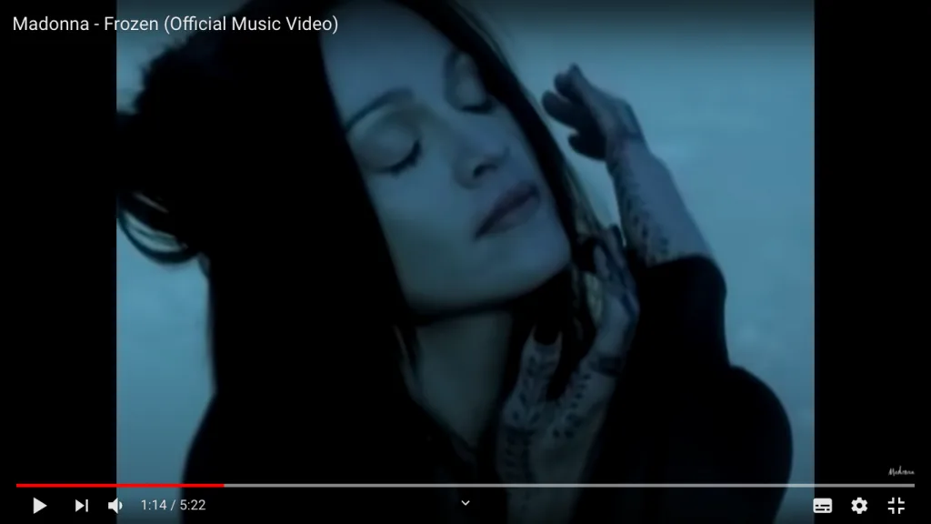 视频截图,标题为'Madonna - Frozen (Official Music Video)',画面中麦当娜双手举至脸颊,手指和手背布满黑色海娜图案,背景为深蓝色沙漠夜景。