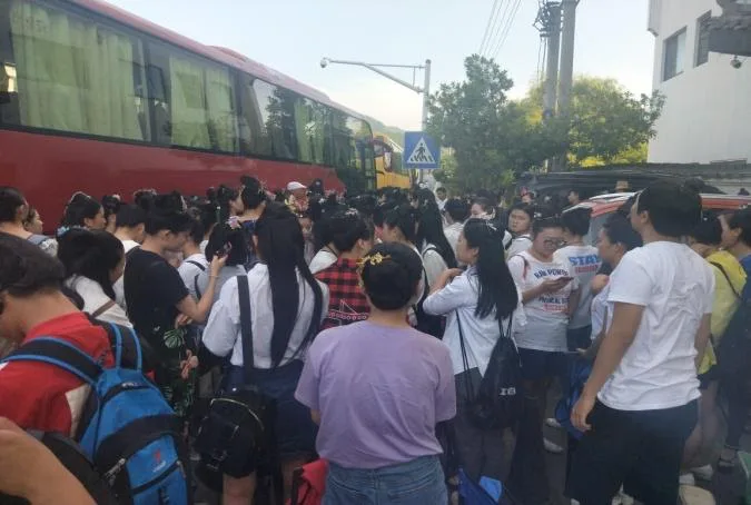 街道上聚集着大批背着双肩包的年轻人,密密麻麻地站在几辆红色大巴车前等候上车。