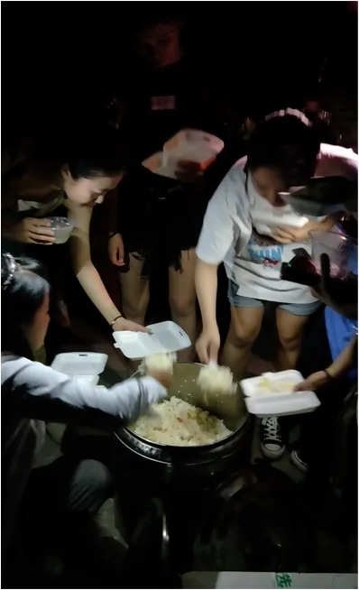 夜间,几名年轻人围着一口大锅,用一次性饭盒盛取里面的饭菜。