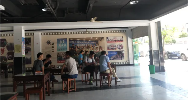 几名年轻男子围坐在室外木桌旁用餐,身后墙面装饰着仿胶片边框的展板,展示着《我是路人甲》相关海报与合影照片。