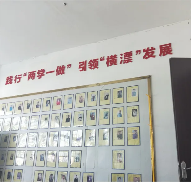 室内墙上红色大字写着'践行'两学一做' 引领'横漂'发展',下方整面墙挂满一格格证件照式的小相框。