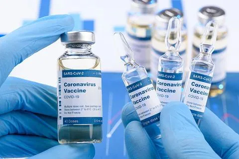 戴蓝色医用手套的双手展示多支贴有“新冠病毒疫苗”标签的小玻璃瓶和安瓿