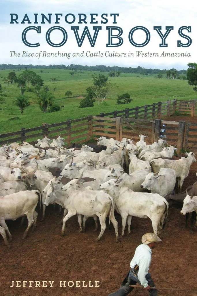 书封面,书名《Rainforest Cowboys》,作者Jeffrey Hoelle,照片为牛仔驱赶一群白牛进入木栅栏围栏,背景是绿色牧场。