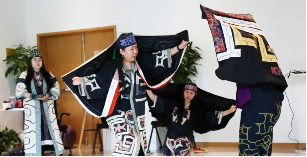 多位身着黑底彩色几何纹样传统长袍、佩戴头巾的表演者围站跳舞，几人张开双臂展开宽大袖摆，动作富有仪式感。