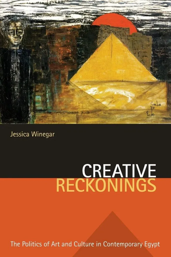 书封《Creative Reckonings: The Politics of Art and Culture in Contemporary Egypt》,作者Jessica Winegar,封面为一幅绘画:黄色金字塔与深色建筑群,上方悬着红色圆日,左侧隐现一个幽灵般的人脸剪影。