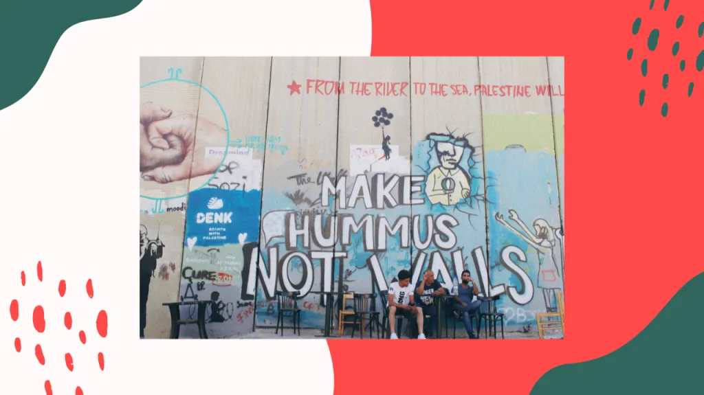 隔离墙前几名巴勒斯坦男子坐在桌旁,身后墙上涂鸦写着'MAKE HUMMUS NOT WALLS'和'FROM THE RIVER TO THE SEA, PALESTINE WILL...',周围还有人像与手势涂鸦。