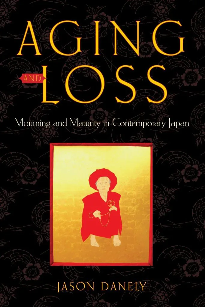 黑底印花封面，中央金色画框里是一位披红衣、戴红帽、蹲坐的老年女性手持念珠，上方印书名《Aging and Loss》与作者 Jason Danely。