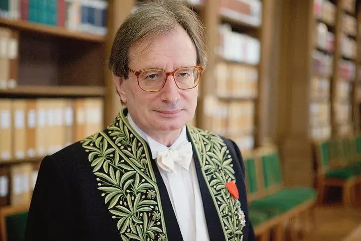 马里翁肖像，戴眼镜，身穿绣有绿色枝叶纹样的学院礼服，站在摆满书籍的图书室内。
