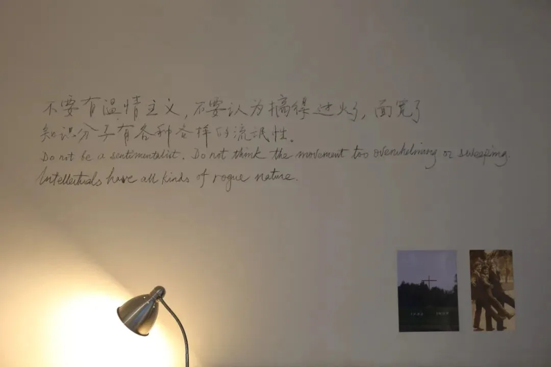 墙上手写着中英文对照的引文:「不能有温情主义,不要认为搞得过火了、面宽了。知识分子有各种各样的流氓性。」墙角亮着一盏台灯,右下角贴着两张小照片。