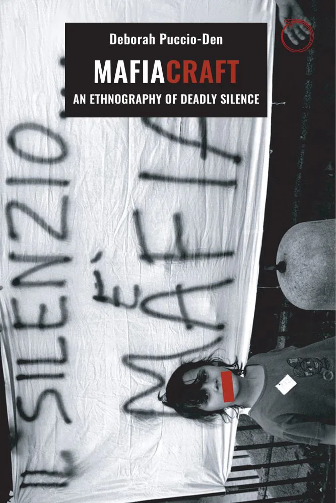 《黑手党之术》（Mafiacraft: An Ethnography of Deadly Silence）封面，作者黛博拉·普奇奥-登（Deborah Puccio-Den）。黑白照片旋转呈横向排布，一块白布上喷涂着意大利语标语「IL SILENZIO È MAFIA」（沉默即黑手党），下方一人的双眼被红色色块遮挡。