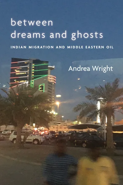 《梦想与幽灵之间》（Between Dreams and Ghosts: Indian Migration and Middle Eastern Oil）封面，作者安德烈娅·赖特（Andrea Wright）。夜色中的城市街景照片，霓虹灯装饰的高楼、棕榈树剪影和停车场，前景有两个模糊的行人身影。