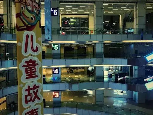 商场中庭俯视三至六层楼层,各层店铺灯光稀疏,几乎不见顾客,前景悬挂着黄色“儿童故事”通道招牌。