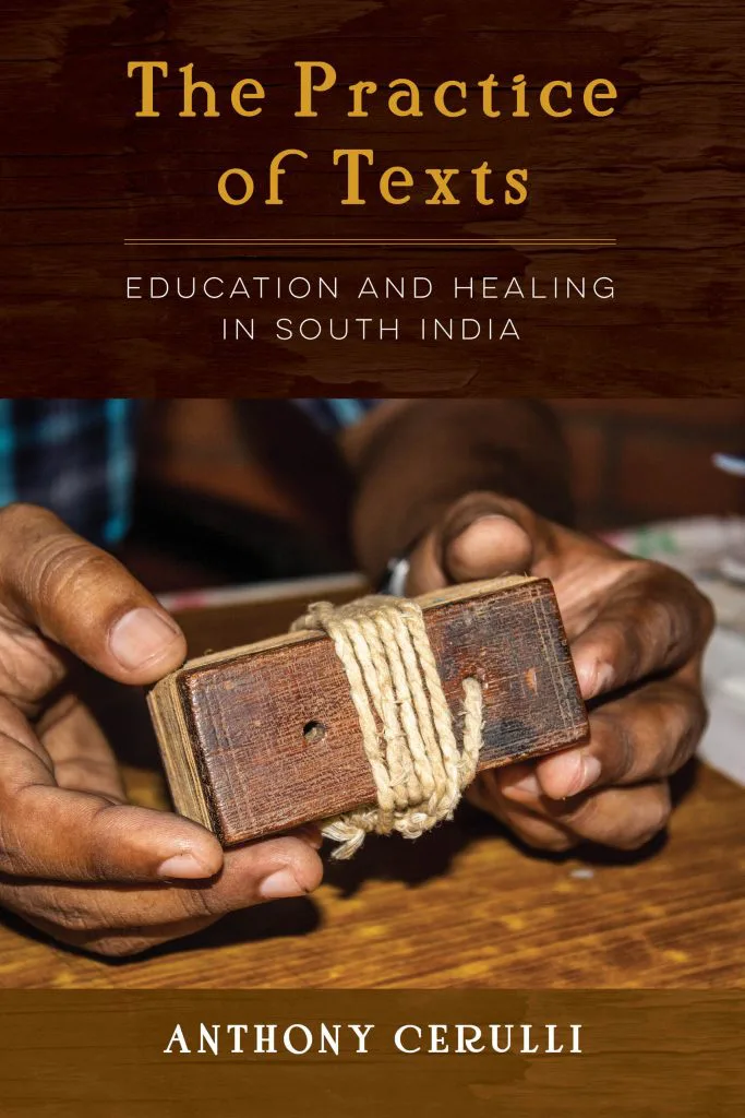 书封《The Practice of Texts: Education and Healing in South India》（文本的实践），作者安东尼·切鲁利，照片是双手捧着一本用麻绳捆扎的木质封面贝叶经典籍。