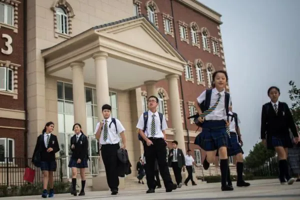 一群穿西式校服、背书包的学生从带罗马柱门廊的教学楼前走出,一名女生正跳跃着奔跑。