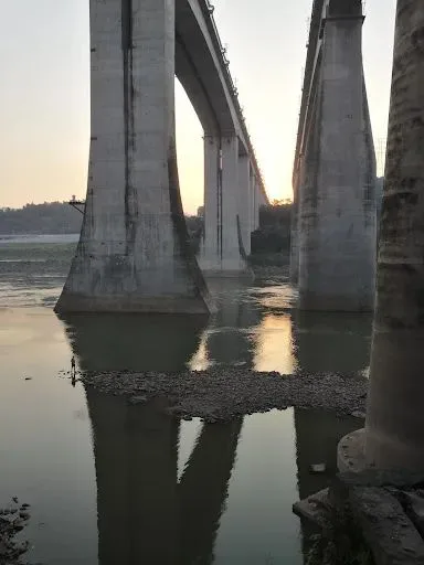 夕阳下几座高大的桥墩矗立在江面上,水中倒映出桥身,江边有一小片碎石滩,一人立于水边。