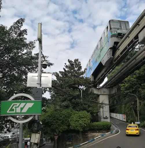 单轨列车在高架轨道上穿行于绿树间,下方是弯曲的马路,路边停着一辆出租车,左侧立着轨道交通标志牌。