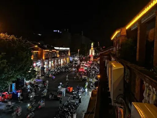 夜晚俯瞰西街,远处钟楼灯光点亮,街道两旁店铺灯火通明,路上停满摩托车,行人熙攘。