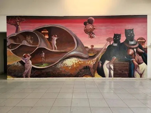 大型壁画描绘一只巨大蜗牛壳内嵌套着裸体人物与建筑场景，画面右侧站立着两个黑豹头人身形象，上方悬浮着形似蘑菇云的球状物，背景是粉红色天空。