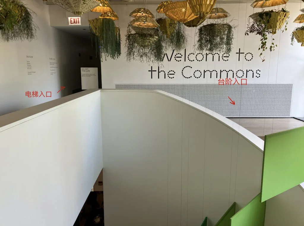 二楼大厅入口,头顶悬挂金色纸灯笼装饰,墙上写着'Welcome to the Commons';红色箭头分别标注'电梯入口'(指向左侧狭窄转角)和'台阶入口'(指向右侧开阔的圆点花纹墙面)。