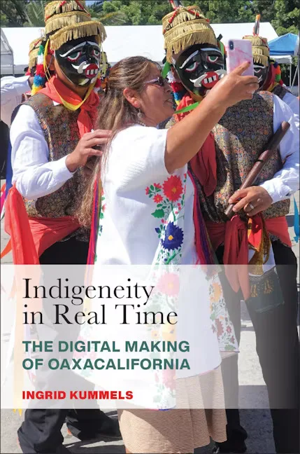 封面书名Indigeneity in Real Time：The Digital Making of Oaxacalifornia，作者Ingrid Kummels；一名穿刺绣上衣的女性举手机自拍，身旁两名男子头戴传统面具和羽饰服装。