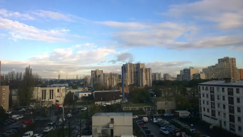 俯瞰视角下的城区全景，多栋高层住宅楼分布在树木和低矮建筑之间，天空多云。