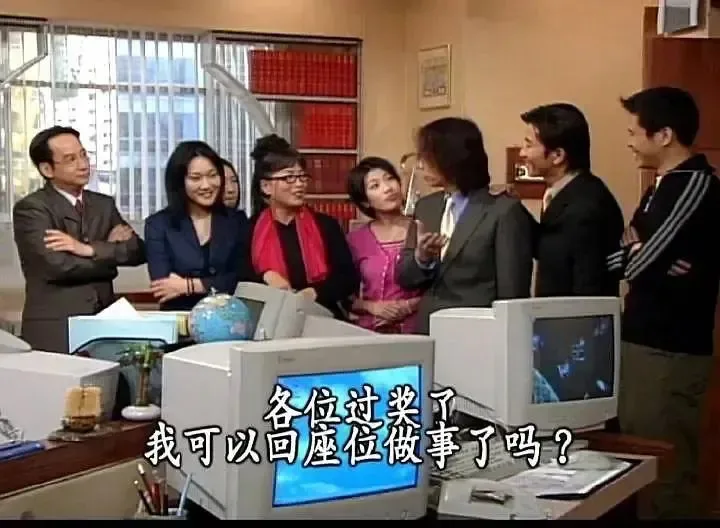 职场剧照配字幕：一群同事围站在办公桌前，中间男子面对众人说话，字幕写着'各位过奖了，我可以回座位做事了吗？'