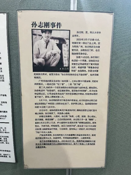 展板题为“孙志刚事件”，左上角为孙志刚坐姿照片，右侧长文讲述他2003年在广州因未携带暂住证被收容后死亡的经过，具体细节文字较小看不清。