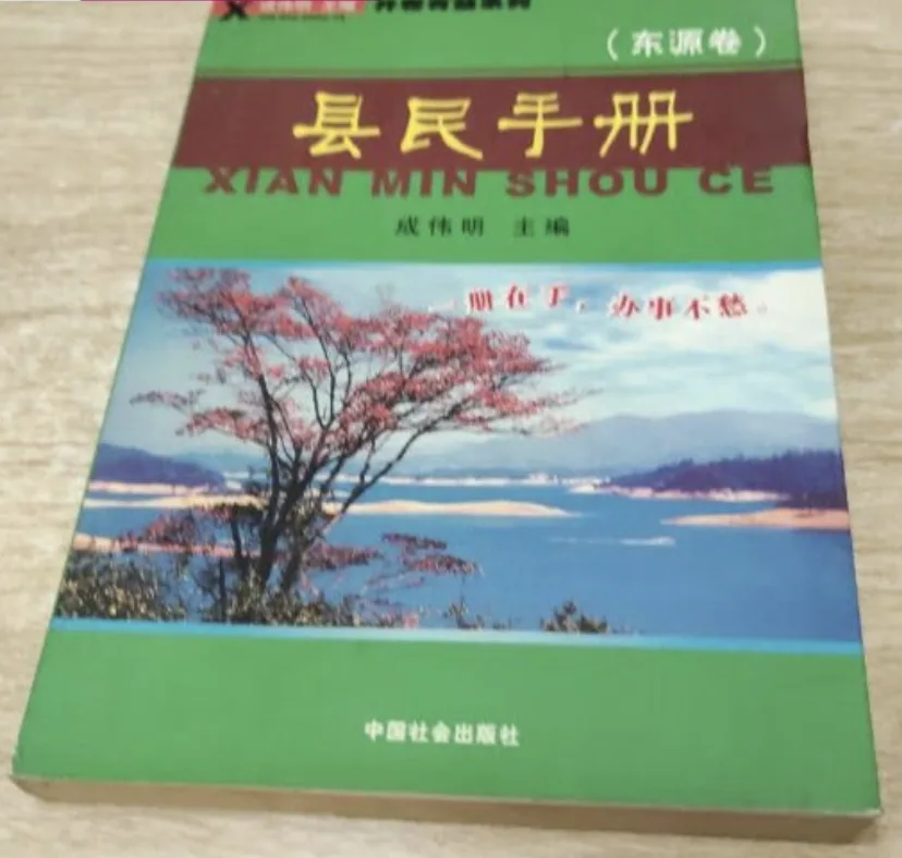封面绿色底，中间嵌一张湖泊与红叶树的风景照，照片上印有红字标语，书名旁标注拼音“XIAN MIN SHOU CE”。